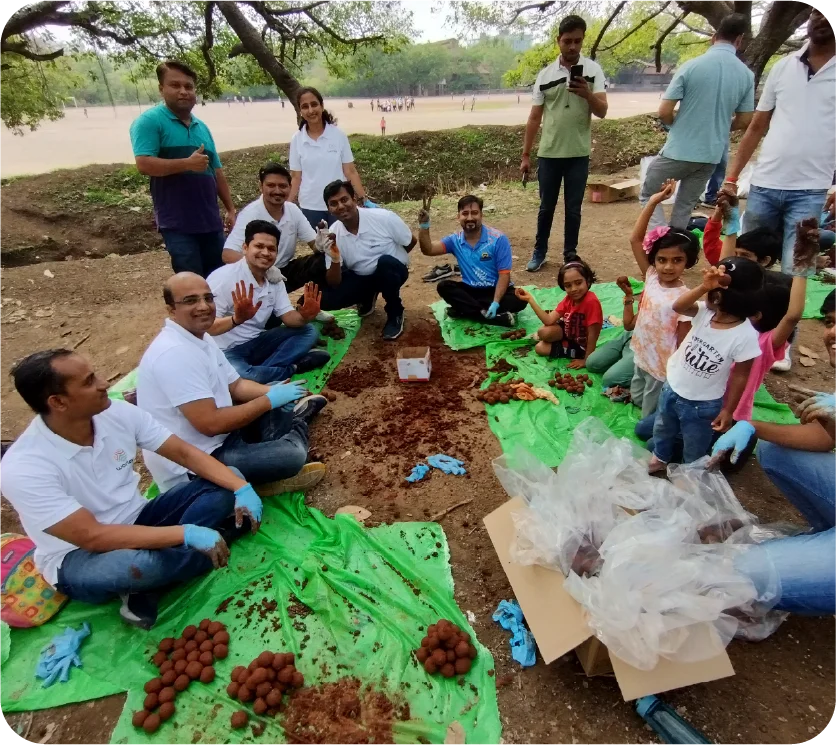 Volunteers sitting together preparing seed balls on a green sheet